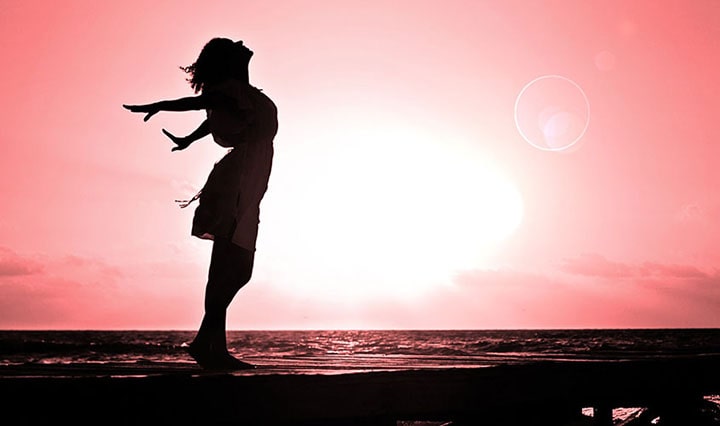 Imagen de una joven en un atardecer en la playa haciendo un movimiento de liberación